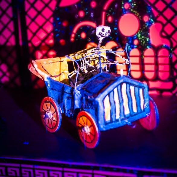 Skelett in einem blauen Auto mit gelben Rädern, alles aus Draht - Key Visual der Ausstellung