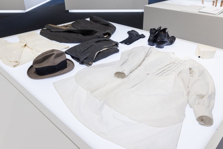 Auf einem weissen Ausstellungstisch liegt eine Herrenausstattung mit Jacke, Hosen, Hemd, Kragen, Weste, Unterhosen, Socken, Filzhut, Schuhen aus Basel, Schweiz  von 1924