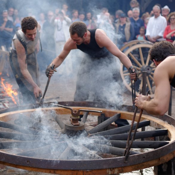 Cinq forgerons cerclent une roue en bois avec une soudure métallique