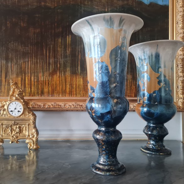 Une pendule dorée et deux vases en porcelaine sur un plateau de marbre gris devant une toile peinte