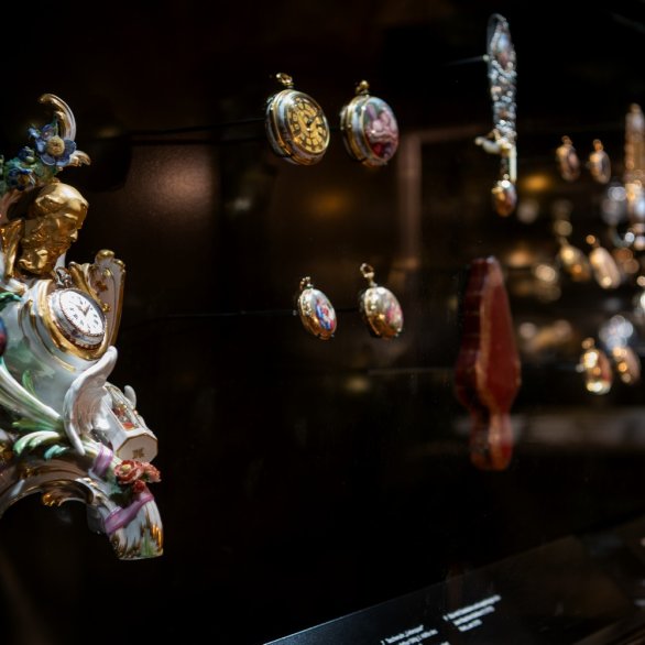 Historische, bunte Taschenuhren in einer Vitrine.