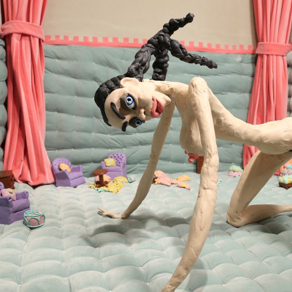 Nathalie Djurberg und Hans Berg Damaged Goods 2019 Nathalie Djurberg und Hans Berg © VG Bild-Kunst, Bonn 2024, Courtesy the artist and Lisson Gallery Nackte Knetfigur einer Frau auf den Knien in einem Raum mit kleinen Möbeln