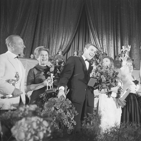 V. l. n. r. mit ihren Bambis in den Händen auf der Bühne in der Schwarzwaldhalle stehend: Heinz Rühmann, Paula Wessely, Götz George, Loni von Friedl, Ruth Leuwerik, Sophia Loren und Rock Hudson, 1962 Schwarz-Weiß-Foto von Filmstars auf einer Bühne mit den Bambi-Filmpreisen in den Händen.