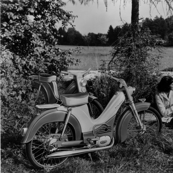 Schwarz-Weiß-Foto von zwei Mopeds links und einem sitzenden Paar rechts.