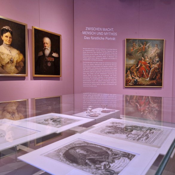 Blick in die Ausstellung mit Gemälden an der Wand und Grafiken in den Vitrinen