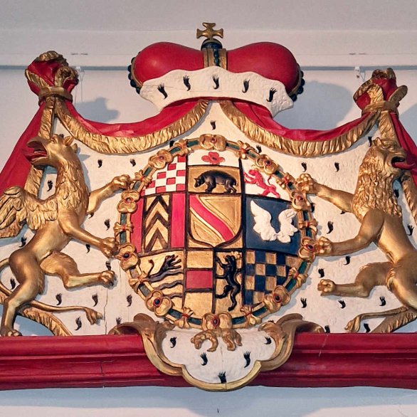 Wappen mit Hermelinmantel und Krone umrahmt, das Wappen selbst zeigt verschiedene Bilder wie Karo oder Streifen, Tiere und Blumen