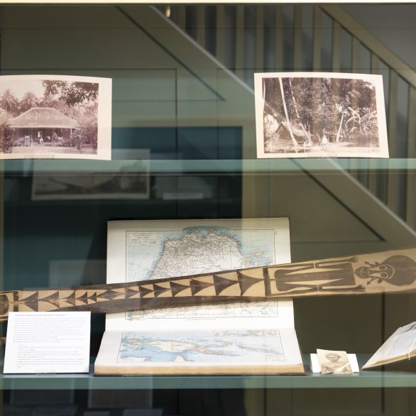 Ausstellungsansicht des aktuellen Schaufenster Archivs mit historischen Fotos, Kartenmaterial und einem Zeremonial-Paddel