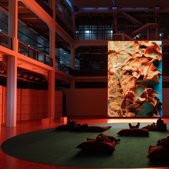 Ein großer Bildschirm, vor dem Sitzsäcke stehen, auf dem menschen liegen.