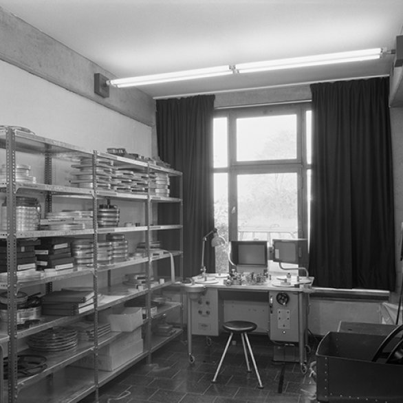 Schwaez-weiß-Fotografie: Raumansicht eines Büros mit einem Regal an der linken Wand und einem Schreibtisch vor einem Fenster.